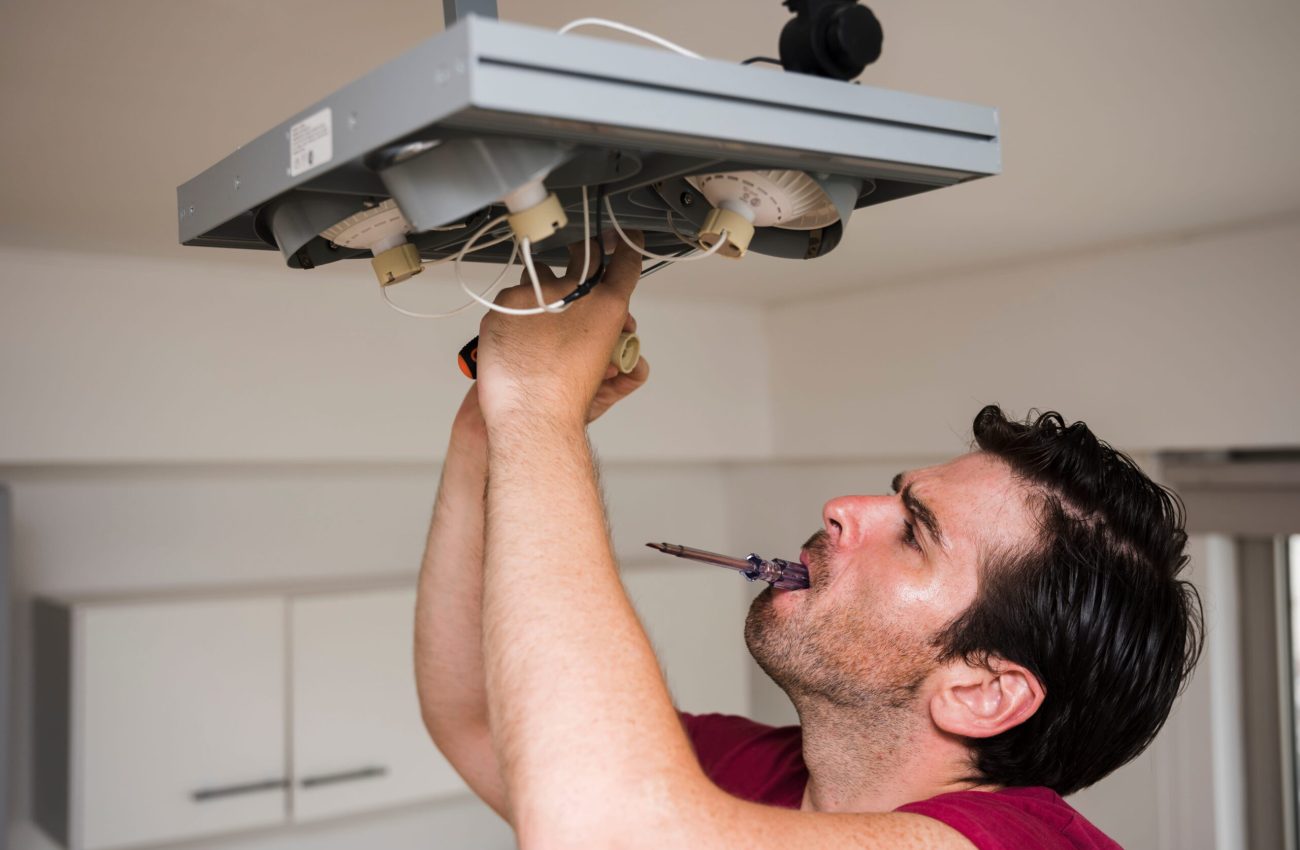 man-carrying-tester-mouth-while-repairing-ceiling-focus-light-home (1)
